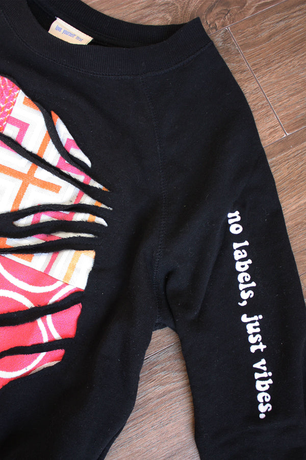 black upcycled sweater with hot pink and orange graphic fabric in the front, repurposed in canada, detail shot of 'no labels, just vibes.' embroidery