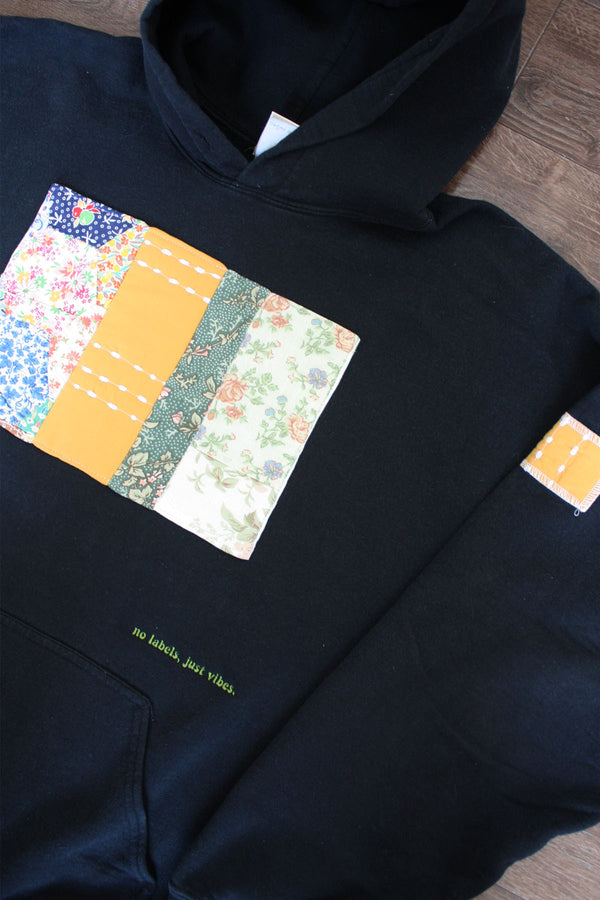 black upcycled hoodie with mustard and green quilt on the front, repurposed in canada, detail shot of 'no labels, just vibes.' embroidery