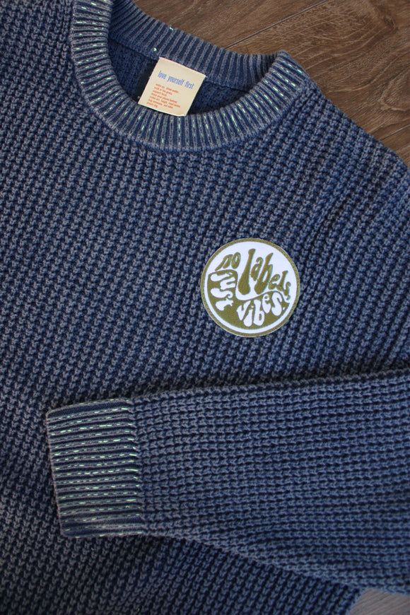 blue knit sweater with visible mending, upcycled in canada, detail shot of 'no labels, just vibes.' patch