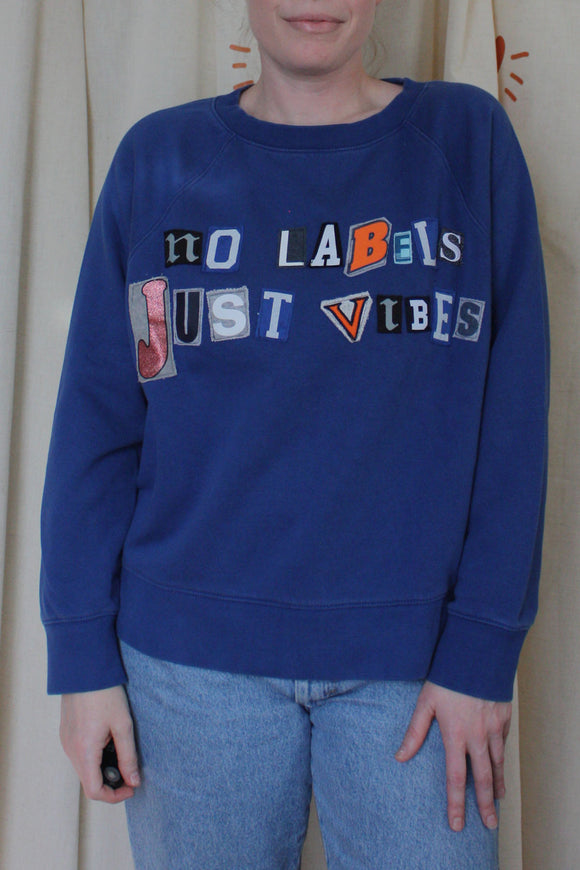 blue upcycled sweater with 'no labels, just vibes.' on the front with ransom letter style lettering, repurposed in canada