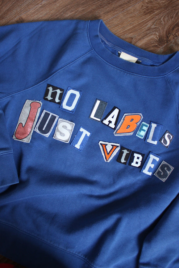 blue upcycled sweater with 'no labels, just vibes.' on the front with ransom letter style lettering, repurposed in canada