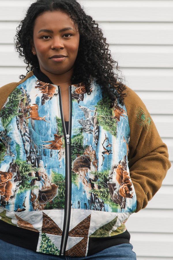 one of a kind bomber jacket that features canadian woodland scenes with a green, brown, and white quilted back. It also features brown wool sleeves with visible mending, repurposed in canada