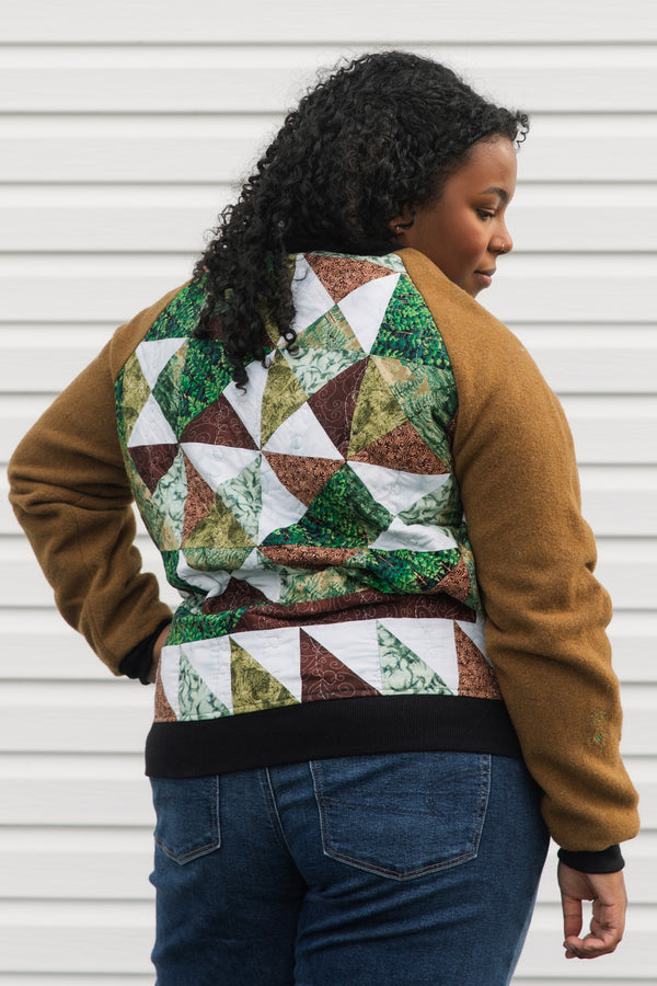 one of a kind bomber jacket that features canadian woodland scenes with a green, brown, and white quilted back. It also features brown wool sleeves with visible mending, repurposed in canada