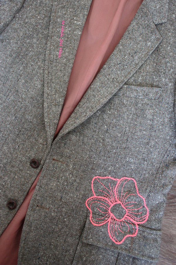 beige/brown upcycled blazer with pink hand embroidered flower, repurposed in canada, detail shot of embroidered peony and 'no labels, just vibes.' embroidery