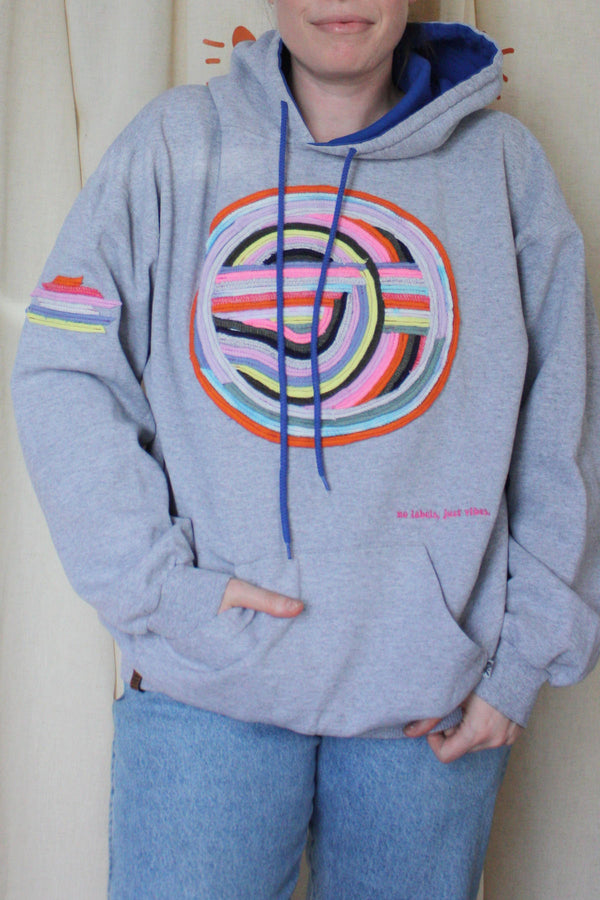 grey hoodie with colourful motif on front, sleeve and hoodie. this upcycled gem is one of a kind and uses sweater seams to bring this design to life. repurposed in canada