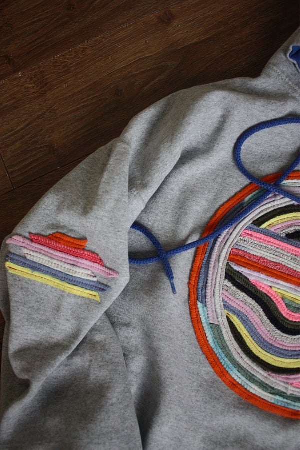 grey hoodie with colourful motif on front, sleeve and hoodie. this upcycled gem is one of a kind and uses sweater seams to bring this design to life. repurposed in canada