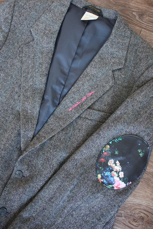 classic dark grey tweed blazer, upcycled with floral faux leather elbow patches, repurposed in canada, detail shot of 'no labels, just vibes.' embroidery