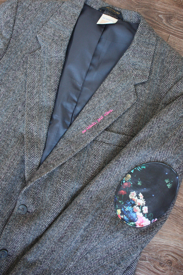 classic dark grey tweed blazer, upcycled with floral faux leather elbow patches, repurposed in canada, detail shot of 'no labels, just vibes.' embroidery