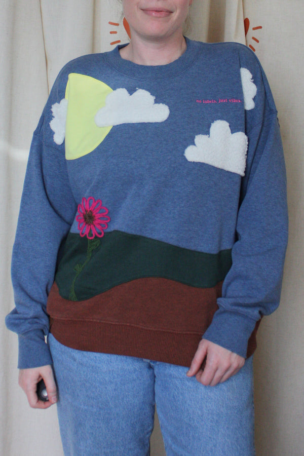 upcycled earth sweater featuring the earth, grass, sky with the sun, clouds  and a flower, repurposed in canada