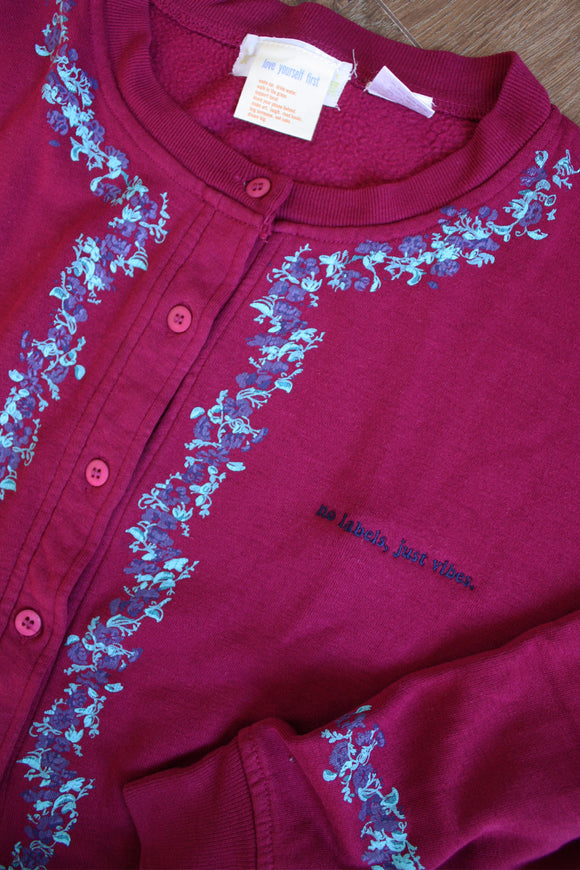 red upcycled button up sweater, with floral details around sleeves and front, repurposed in canada, detail shot of 'no labels, just vibes.' embroidery