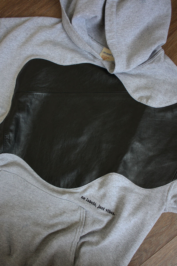 grey upcycled hoodie with black leather detailing, repurposed in canada, detail shot of 'no labels, just vibes.' embroidery