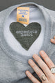 smaller 'conscious heart' at back neck of light grey sweater, unisex and oversized fit