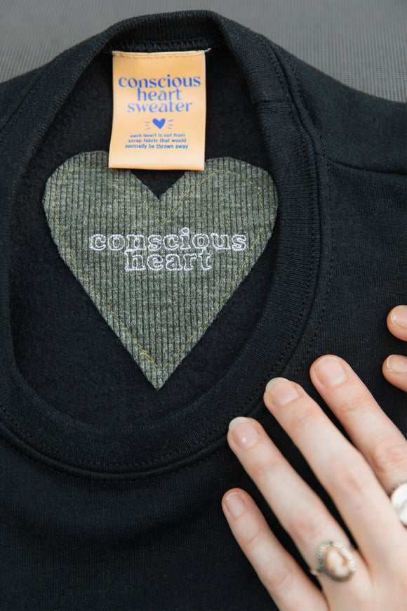 small conscious heart stitched onto back neck of black sweater, unisex and oversized fit, sewn in canada