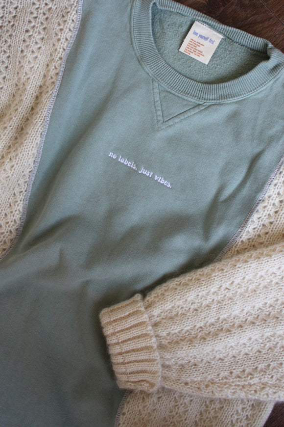 green and cream knit crewneck sweater, upcycled in canada, detail shot of 'no labels, just vibes.' embroidery