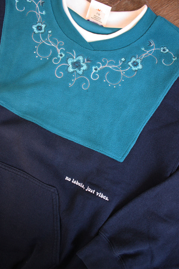 teal and navy upcycled sweater with kangaroo pocket, repurposed in canada, detail shot 'no labels, just vibes.' embroidery