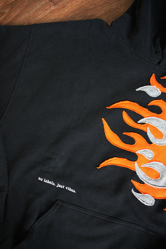 upcycled black fire hoodie with orange and grey, repurposed in canada, detail shot of 'no labels, just vibes.' embroidery