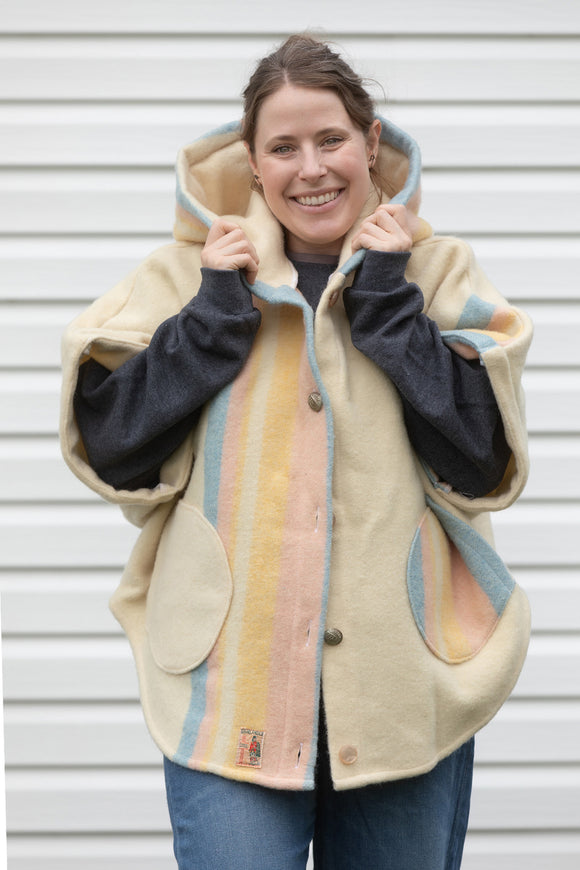 cream, pink, blue and yellow wool blanket upcycled into the clare poncho featuring a big hood, pockets and oversized fit, upcycled and made in canada