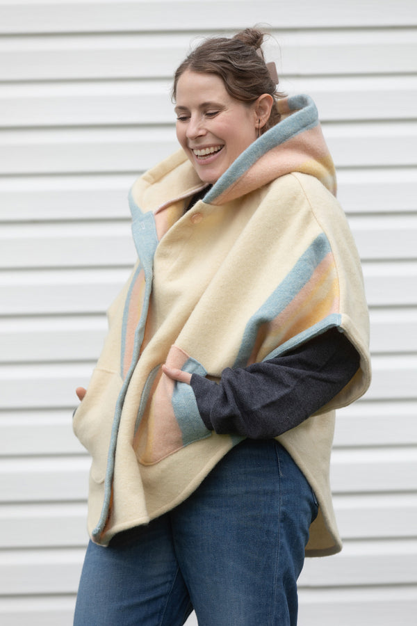 cream, pink, blue and yellow wool blanket upcycled into the clare poncho featuring a big hood, pockets and oversized fit, upcycled and made in canada