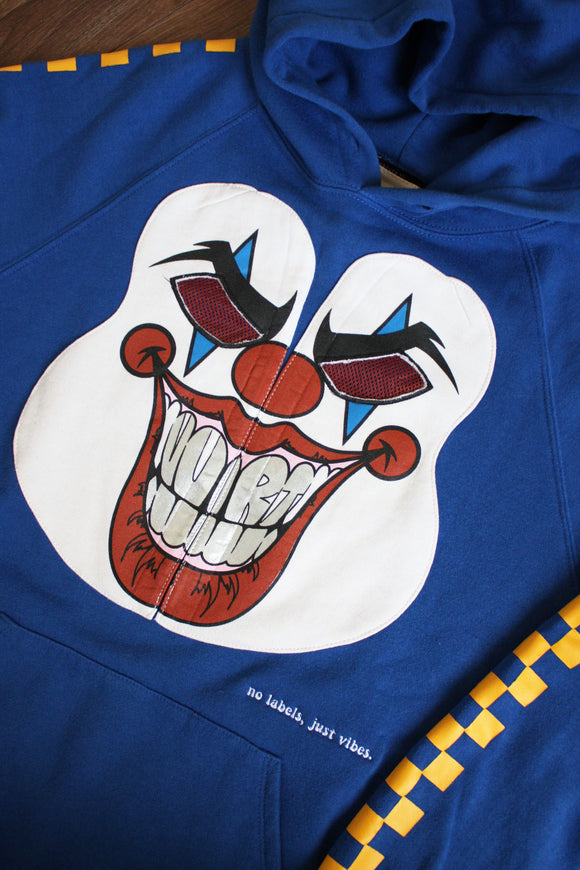 blue hoodie with wrestler mask graphic on the front and a yellow checkered pattern down the sleeves, repurposed in canada, detail shot of 'no labels, just vibes.' embroidery